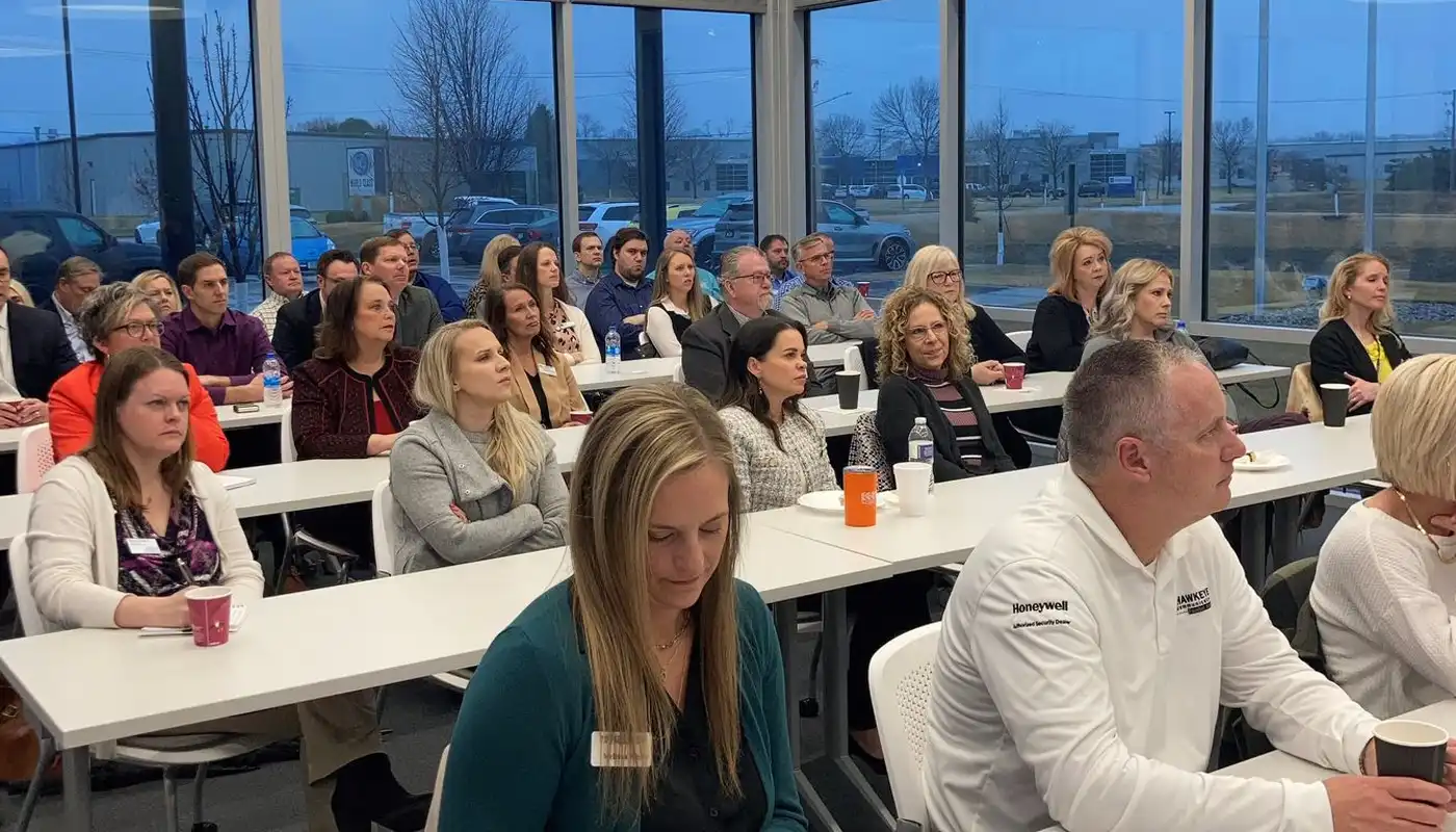 A group of people sit in rows at tables for a business experience