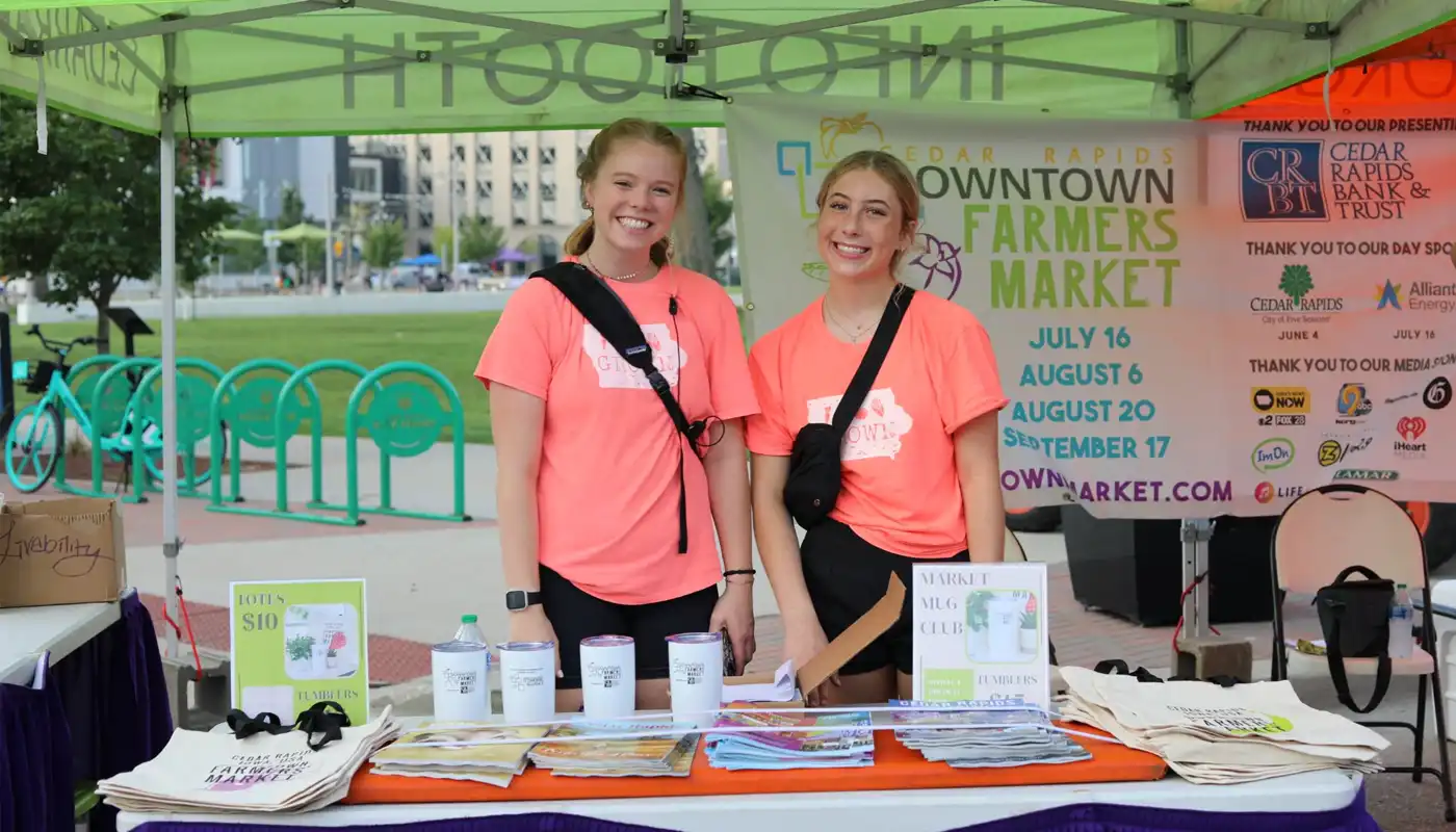 Two young volunteers operate a booth at the Cedar Rapids Farmers' Market