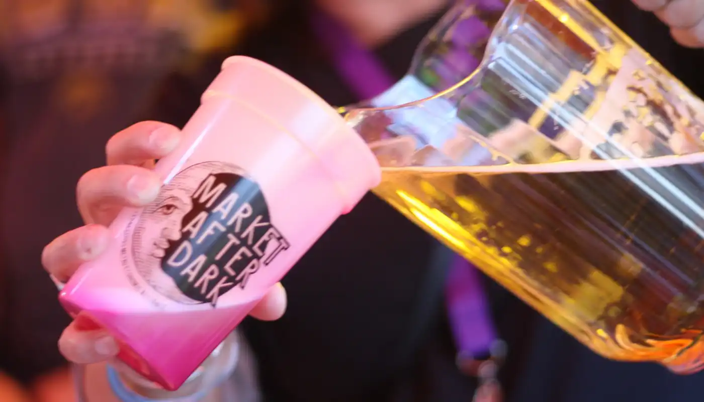 A volunteer pours beer into a Market After Dark glass