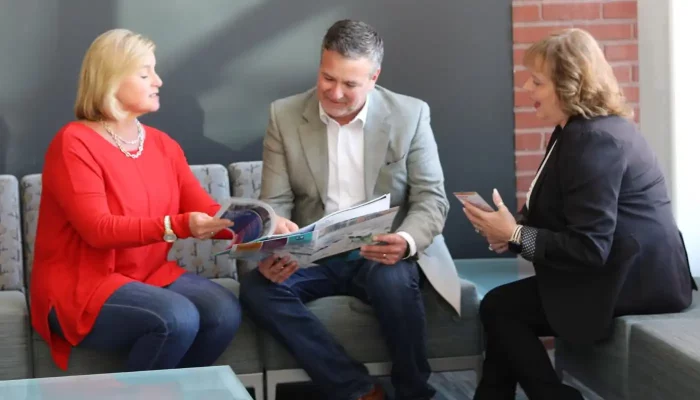Three people sit on lobby couches and look at a magazine report