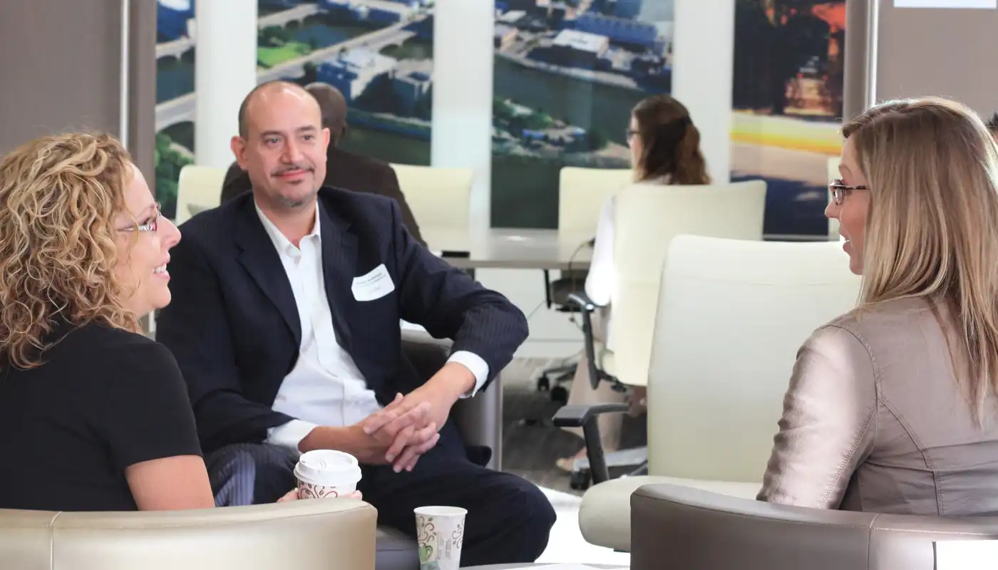 Business colleagues discuss items sitting in white chairs in an open lobby