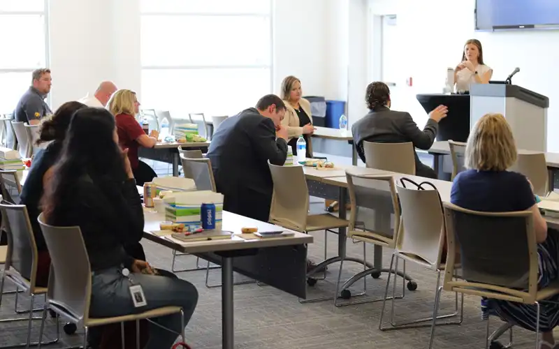 A teacher leads a group learning sessions with people are rows of desks