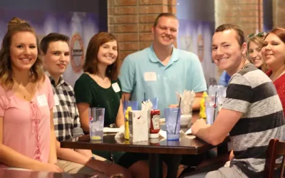 A group of young people sitting around a table smiling at the camera