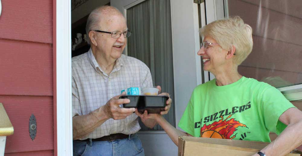 A volunteer delivers a meal to an elderly gentleman