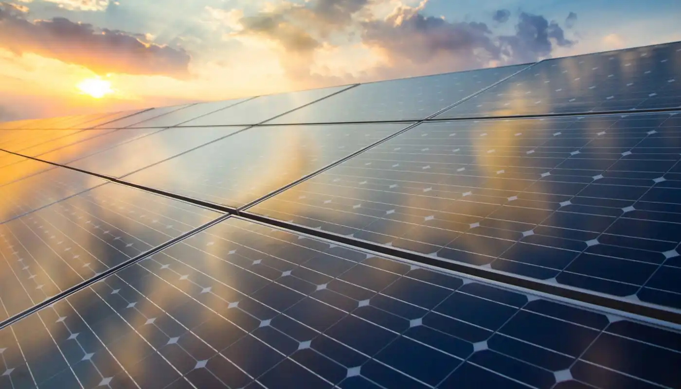 A closeup of a solar panel with the sun bright and orange in the distance