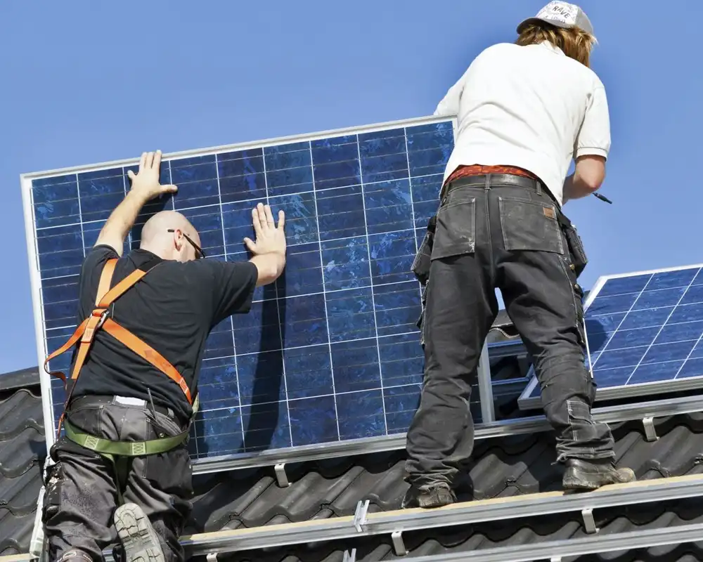 Two workers install a solar panel on a roof