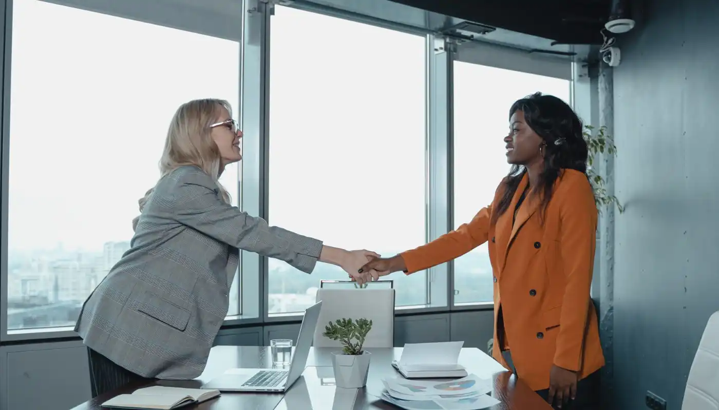Two women shake hands in an office building with a view