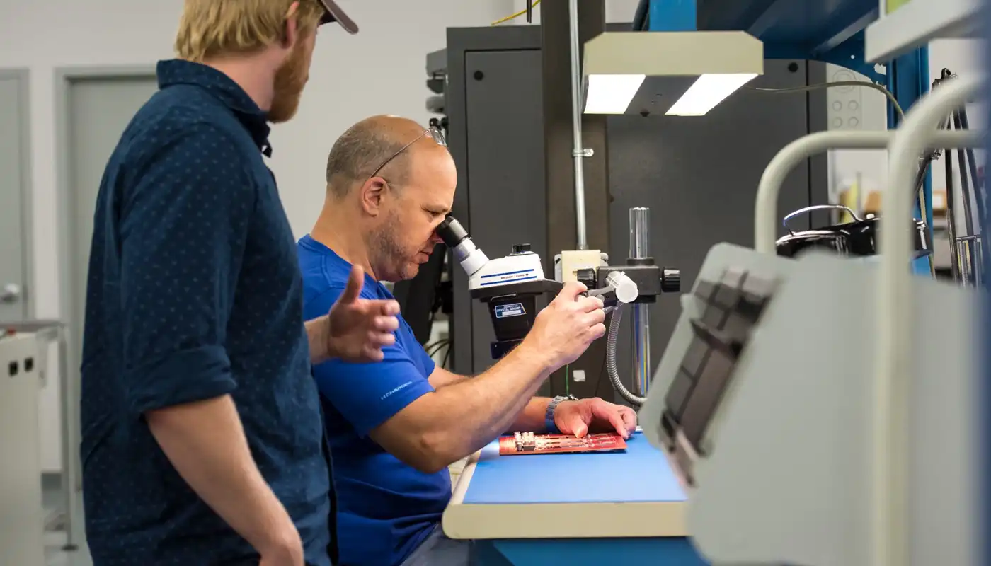 Two people work and look through a microscope